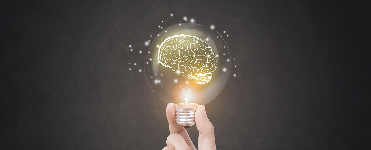 Image of hand held light bulb illuminating with the image of a lit brain inside the bulb  