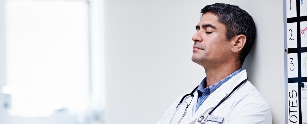 Image of physician leaning up against a wall to rest.