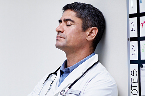 Image of physician leaning up against a wall to rest.