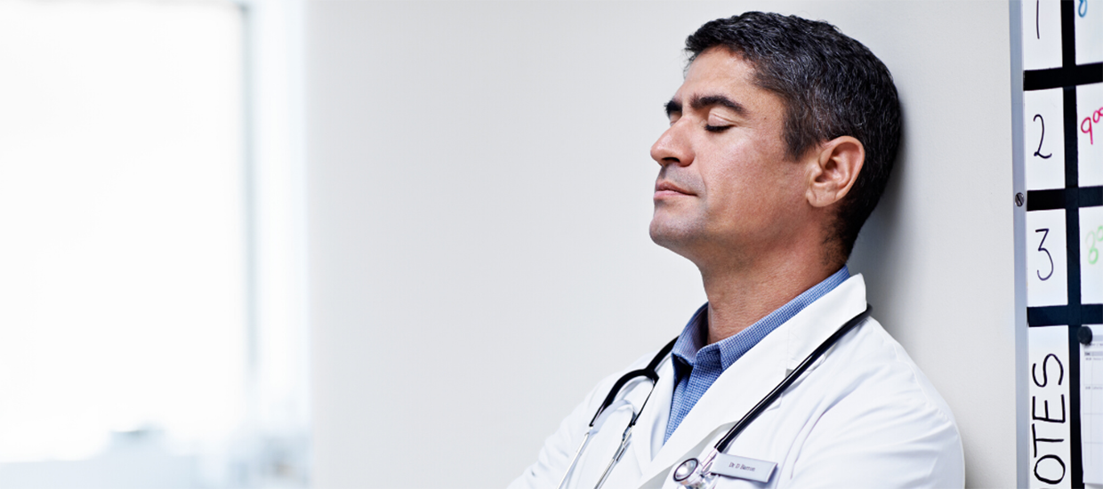 Image of a physician leaning up against a wall to rest.